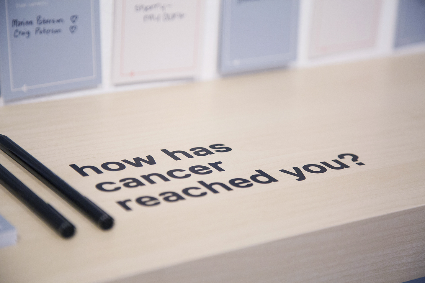 Black letters on a wooden shelf ask visitors 'how has cancer reached you?'